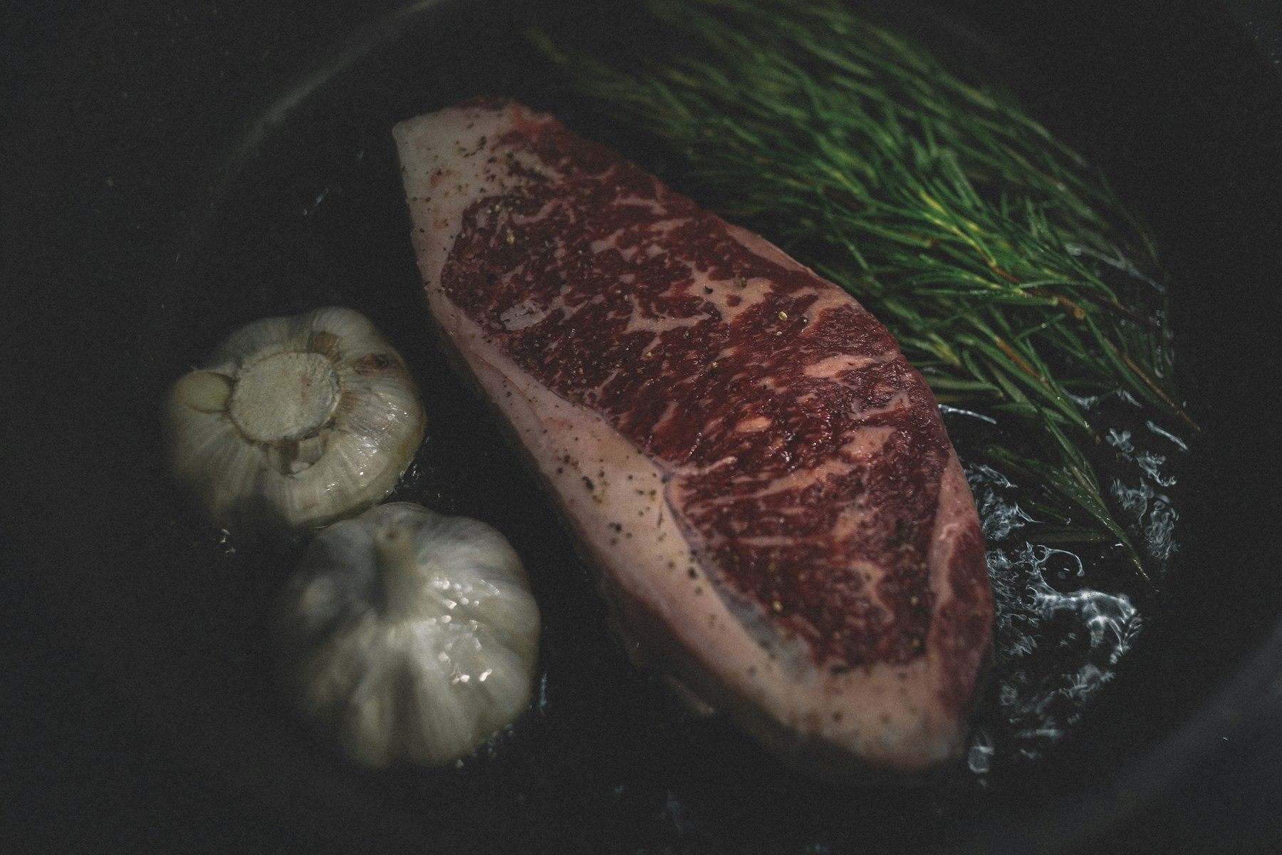 Highly marbled steak cooking in a pan with garlic and rosemary