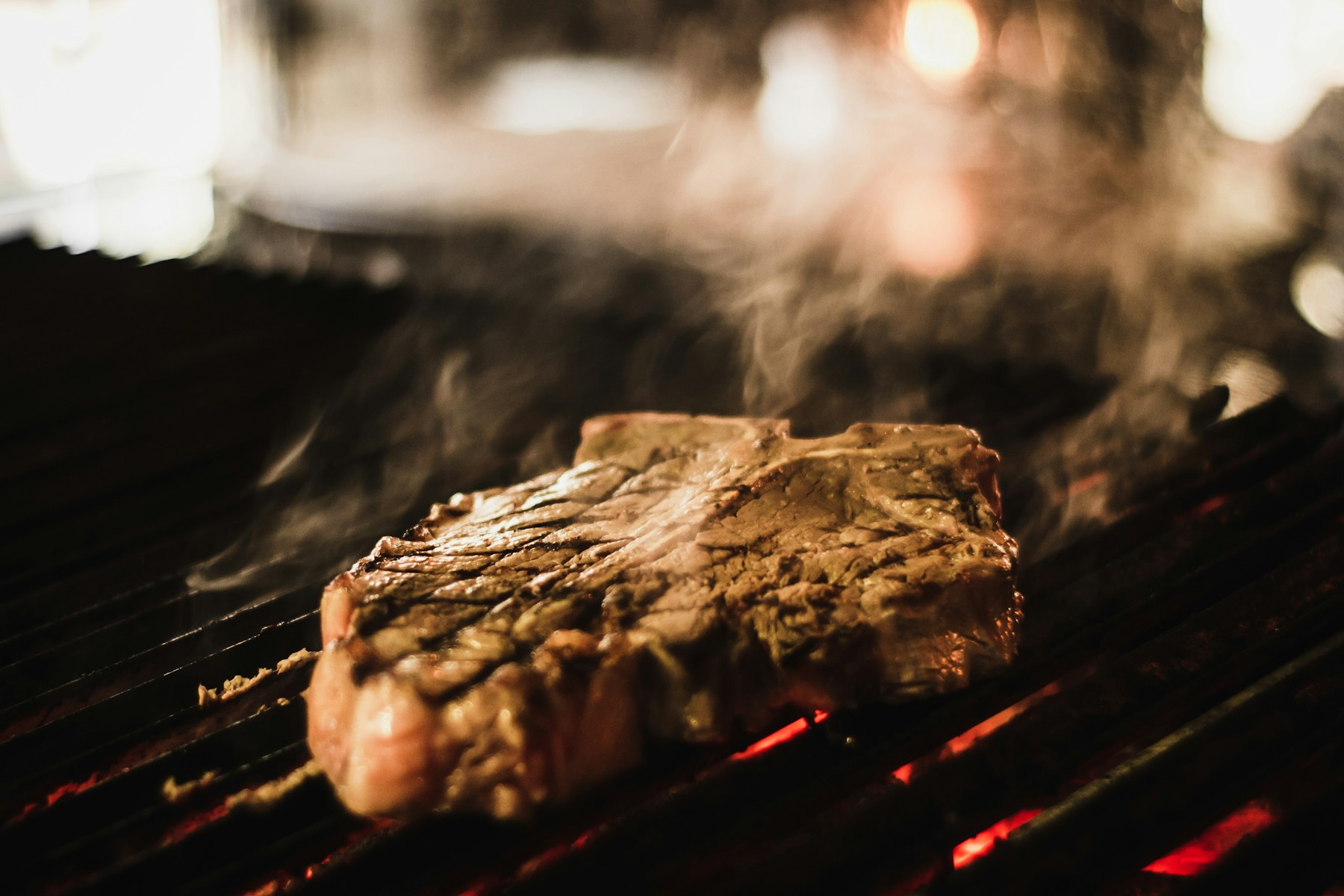 Steak cooking on a smoky charcoal grill
