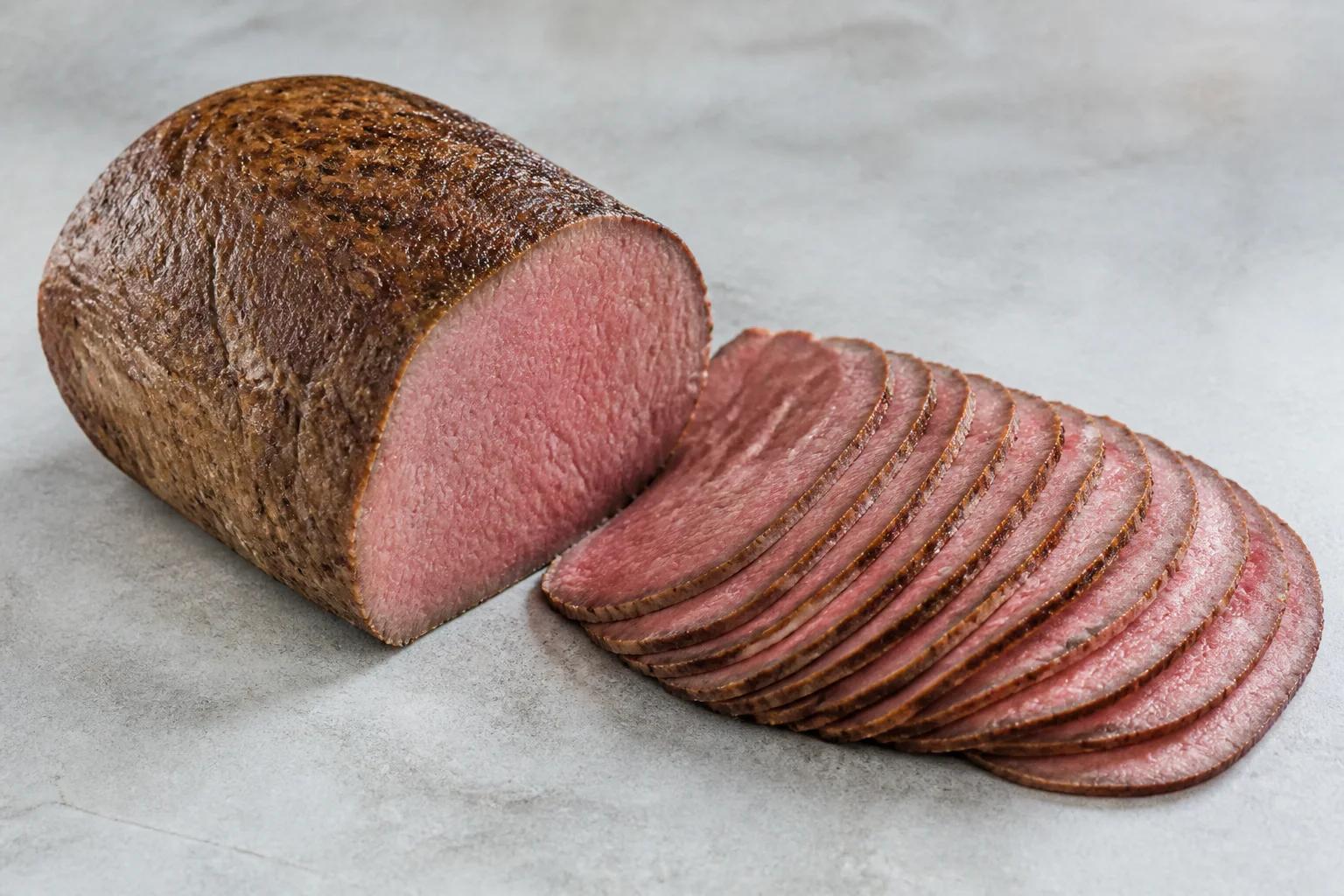 Lean eye of round roast carved into thin rosy cross-grain slices